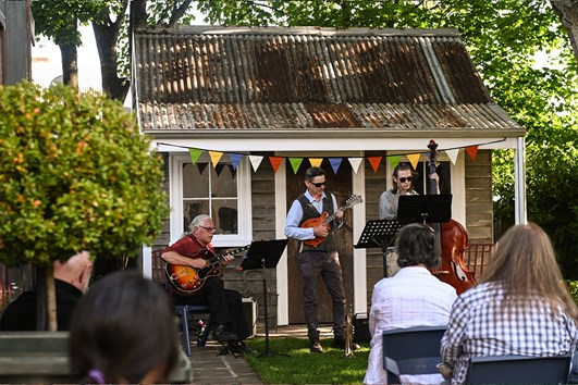 Musical trio performing on a verandah to an audience sitting in a garden at Verandah Music Festival