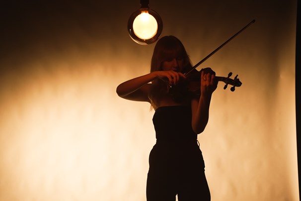 Emma Greenhill plays violin in moody lighting.