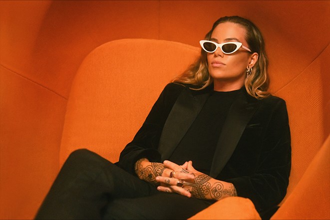 Songwriter Tash Sultana sitting in an orange chair with white sunglasses
